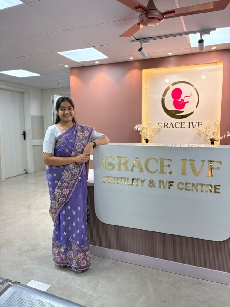 A woman in a purple saree standing and smiling at the Grace IVF reception area.