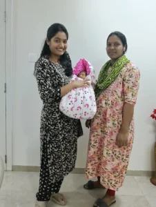 Two women smiling while holding a newborn baby wrapped in a blanket.
